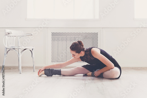 Classical ballet dancer stretching in white training class