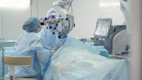 A surgeon and his assistant observe their actions through a microscope. 