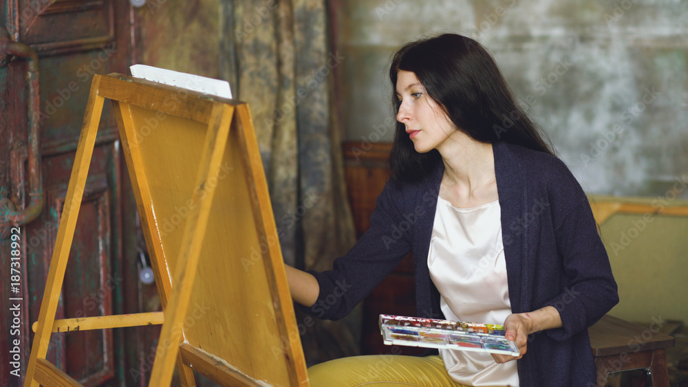 Obraz premium Young woman artist draw pictrure with watercolor paints and brush on easel canvas