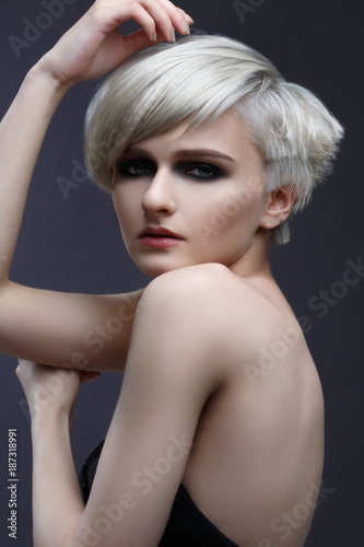 Fashion beauty portrait of a blonde girl with a stylish short haircut on a gray background.