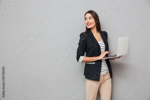 Smiling asian business woman holding laptop computer and looking back