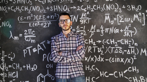 Young scientist man posing in chemical and mathematical equations wall room interior © silverkblack