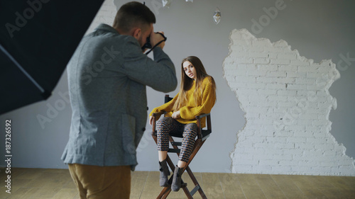 Young beautiful woman model posing for photographer while he is shooting with a digital camera in photo studio indoors photo