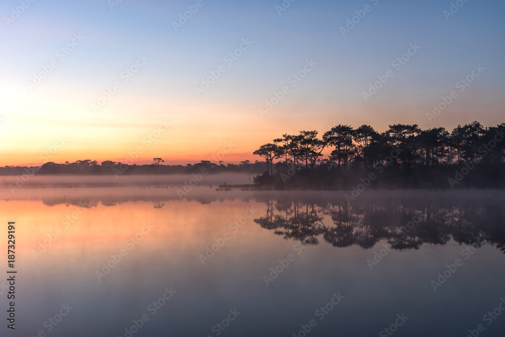 Morning sunrise over the lake with silhouette pinf forest reflect on water surface at Phu Kradaung, national park in Thailand.