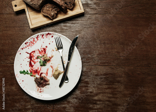 Dirty plate with eaten food,and folded cutlery with a bread board on a wooden table