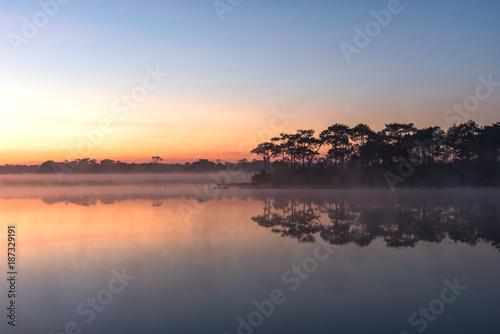 Morning sunrise over the lake with silhouette pinf forest reflect on water surface at Phu Kradaung, national park in Thailand.