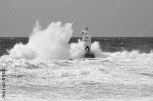 White lighthouse on the cliff. Lighthouse Mangiabarche situated in the south of Sardinia. Italy. Black and white, grey sky, white wave.