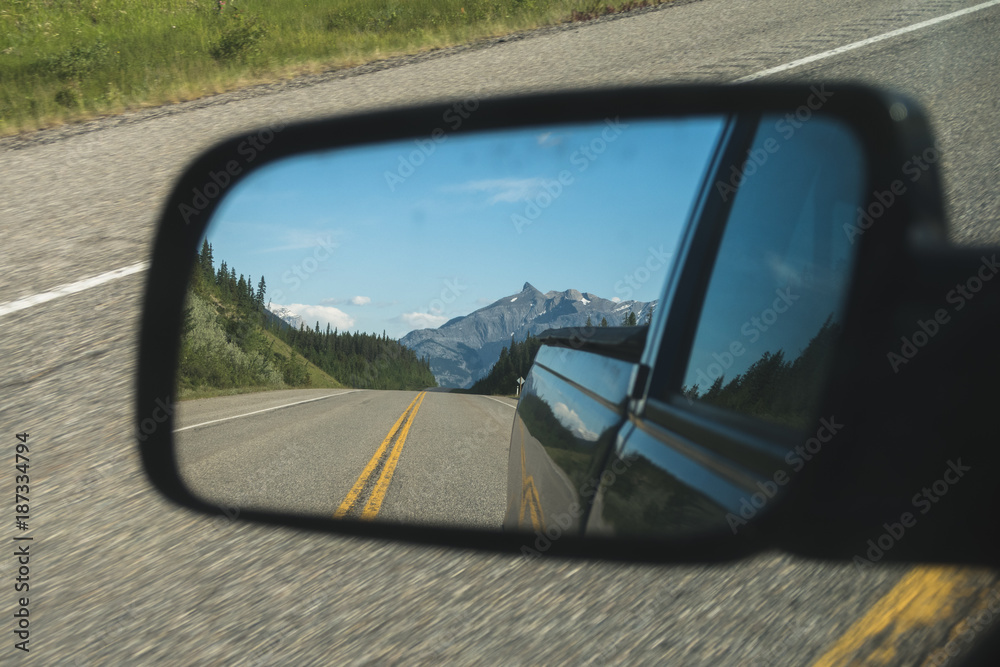Reflection of mountain in side mirror. Driving away from a mountain you can see the road with two yellow painted lines leading to the mountain. 