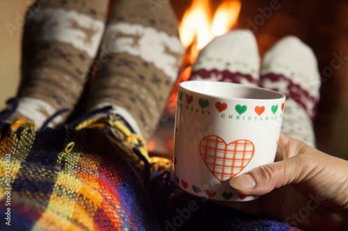 Fototapeta Naklejka Na Ścianę i Meble -  Man and woman in warm knitted socks with cups of hot drink in front of the fireplace