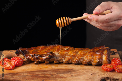 Cooking pork rib chops with honey sweet sauce on dark wooden background. The chef pours honey pork ribs. With copy space photo