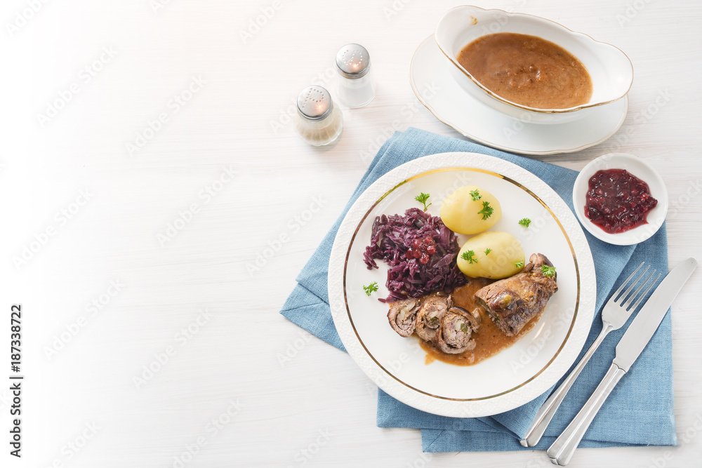 beef roll or roulade with red cabbage, potatoes and sauce on a blue napkin on a bright table, background fades to white, high angle view from above, copy space