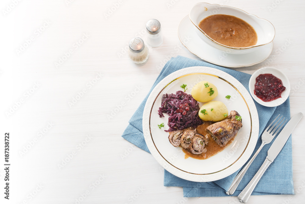 beef roll or roulade with red cabbage, potatoes and sauce on a blue napkin on a bright table, background fades to white, high angle view from above, copy space beef roll or roulade with red cabbage, potatoes and sauce on a blue napkin on a bright table, background fades to white, high angle view from above, copy space
