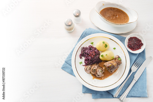 beef roll or roulade with red cabbage, potatoes and sauce on a blue napkin on a bright table, background fades to white, high angle view from above, copy space