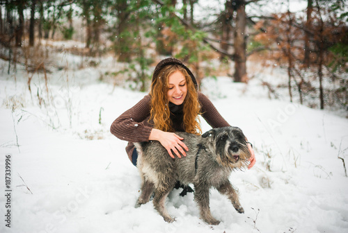 curly haired red-haired girl on a walk with a dog schnauzer in the winter afternoon in the forest