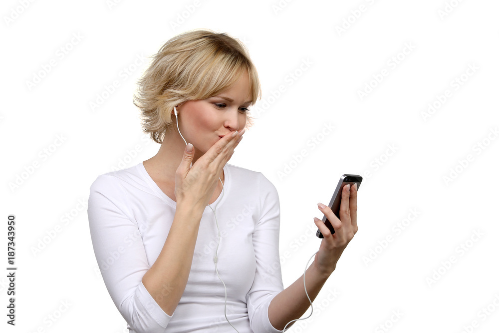 Hübsche blonde Frau mit Kopfhörern schaut in ihr Smartphone Display und wirft einen Luftkuss Hübsche blonde Frau mit Kopfhörern schaut in ihr Smartphone Display und wirft einen Luftkuss