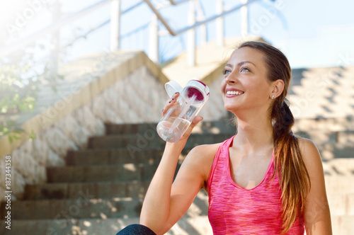 Sporty woman drinking water after jogging