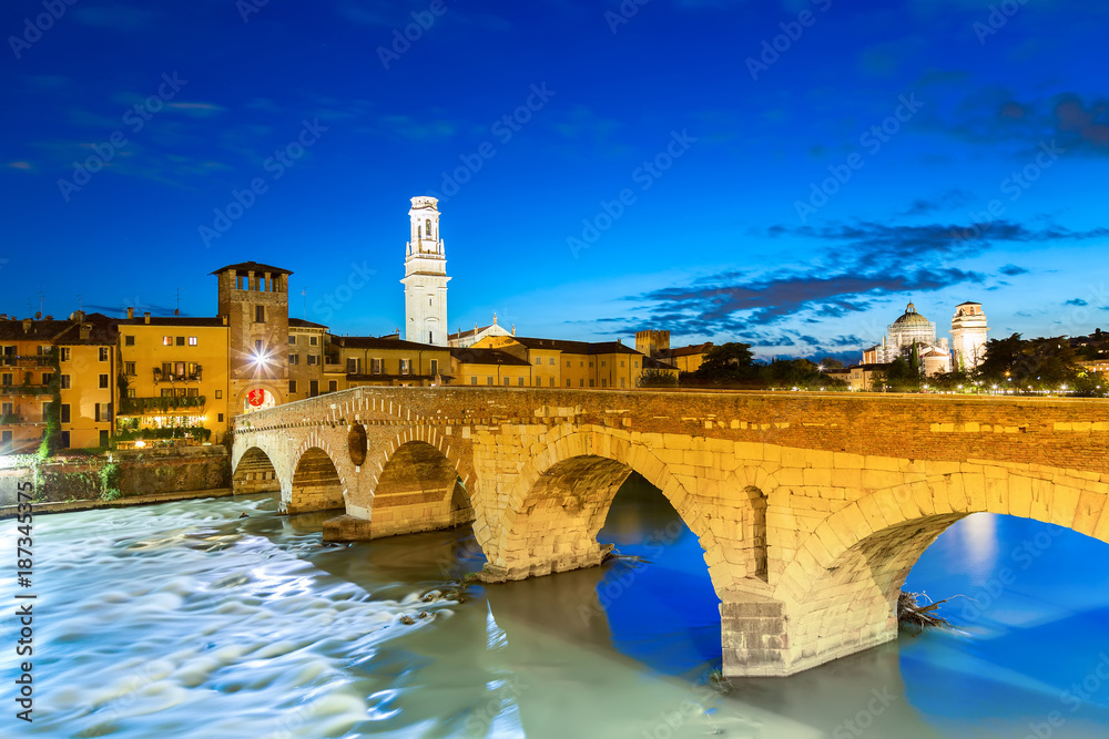 Famous Verona landmark. Ponte di Pietra over Adige river during evening sunset blue hour.