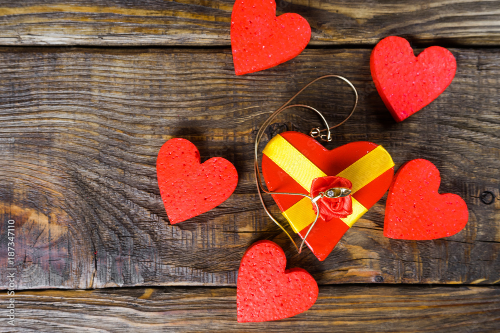Fototapeta premium gift box in the shape of hearts tied with ribbon with a bow in the form of a rose in the center of which lies the Golden slipper with briliant. Around red decorative hearts on wooden background
