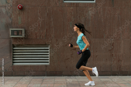 Side view of sporty young woman running on a sidewalk.