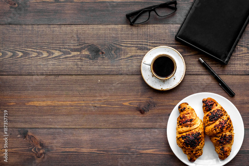 Work at breakfast. Coffee and croissants near notebook and glasses. Dark wooden background top view copyspace
