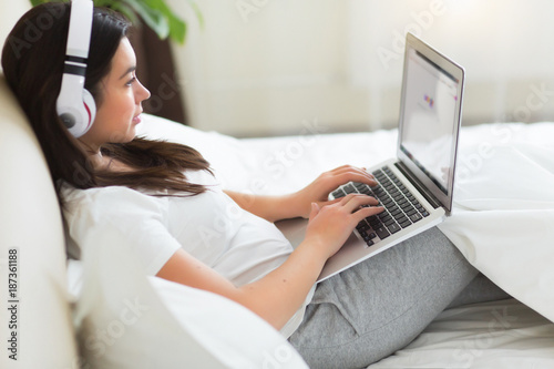 Young pretty woman has a rest on the bed with laptop and listing a music