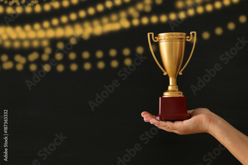 low key image of a woman holding a trophy cup over dark background.