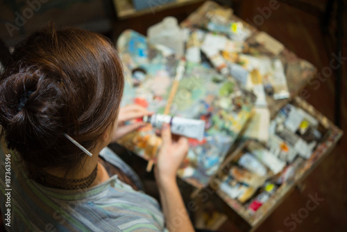 Young woman artist painting with oil paints in the studio workshop