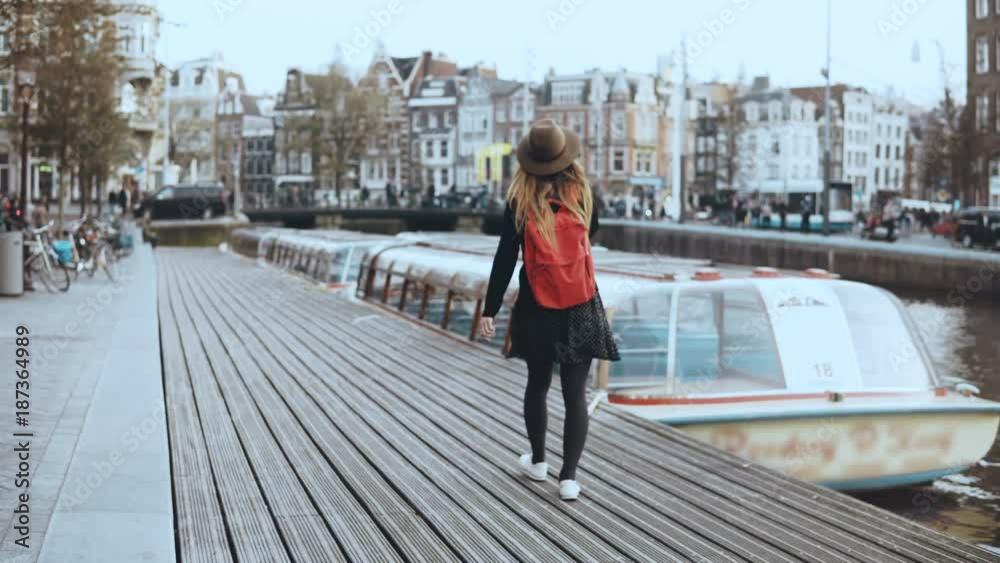 Cute tourist female walks, talks on the phone. Happy relaxed traveler walking along river boat embankment. 4K back view. Cute tourist female walks, talks on the phone. Happy relaxed traveler walking along river boat embankment. 4K back view.
