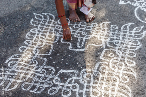 Unidentified indian woman seen drawing kolam (in tamil language) or rangoli using white colored rice during festival season