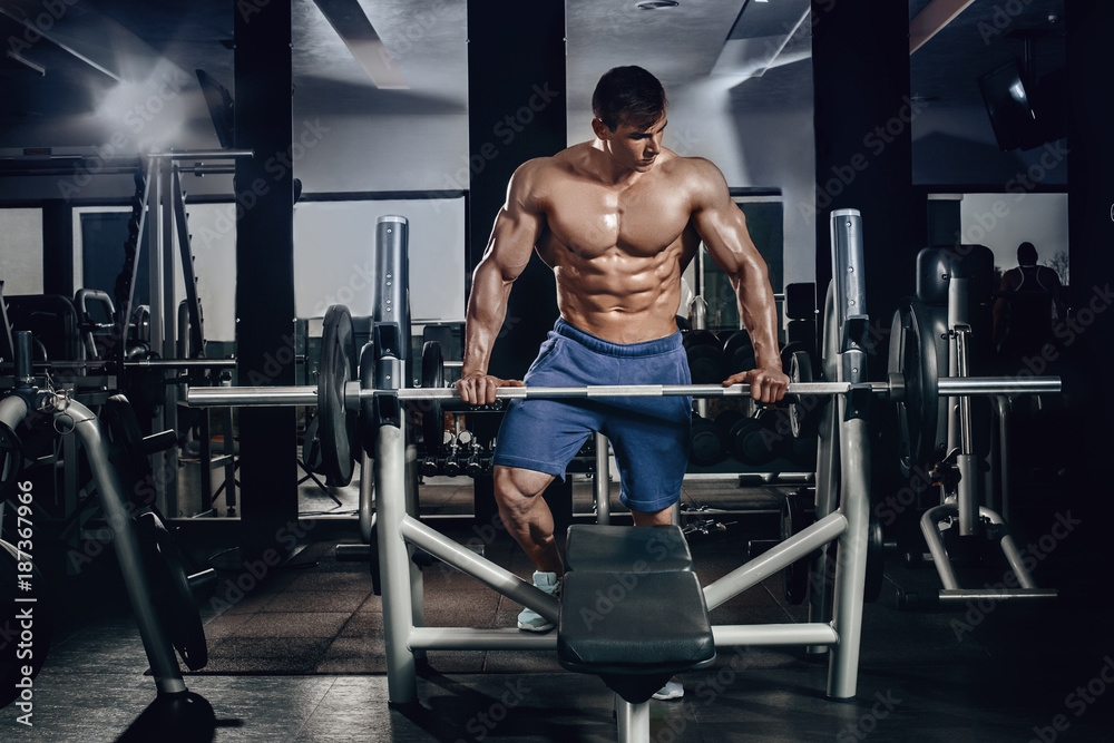 Handsome power athletic man on diet training pumping up muscles with dumbbell and barbell. Strong bodybuilder, perfect abs, shoulders, biceps, triceps and chest