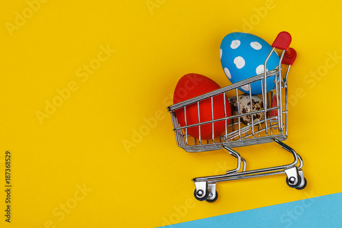 Multicolored easter eggs in a trolley with space for text on a yellow background, top view