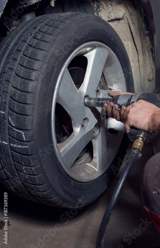 Professional car mechanic working with pneumatic wrench in auto service.