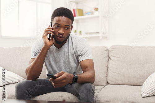 Young man watching tv and talking on mobile in living room
