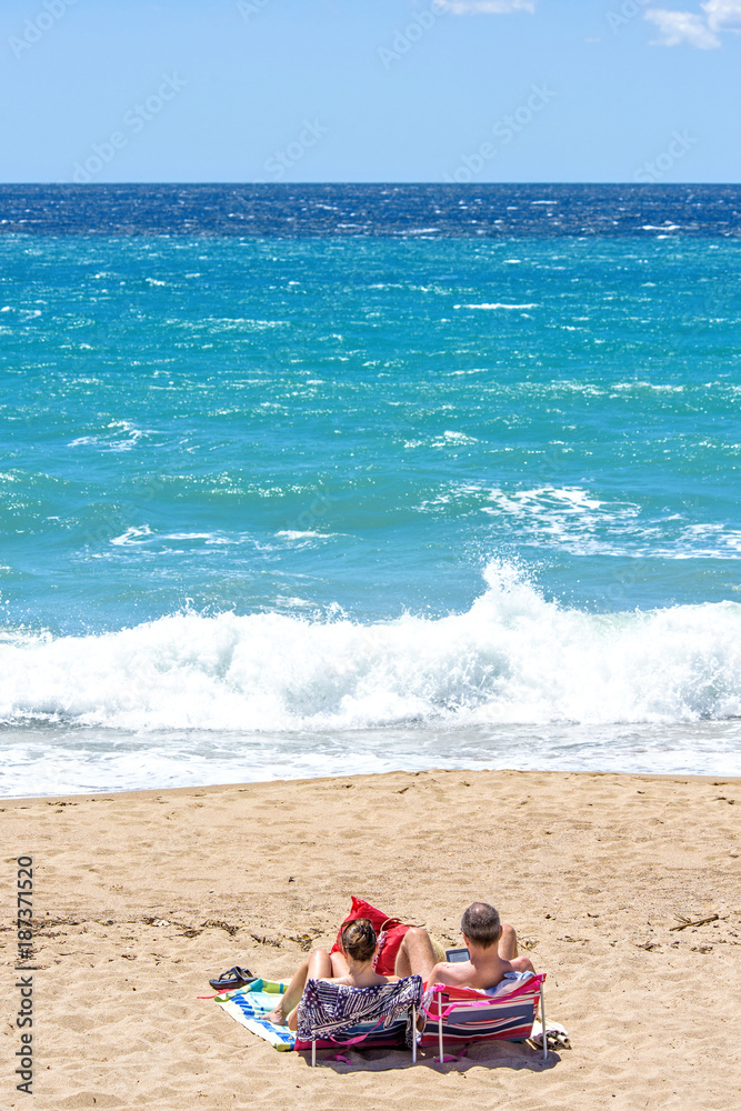 Two mature husband and wife sitting on sunchairs reading books Two mature husband and wife sitting on sunchairs reading books