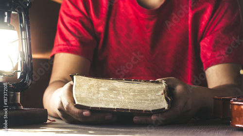 Vászonkép man hands holding holy bible on wooden table with lantern light, christian backg