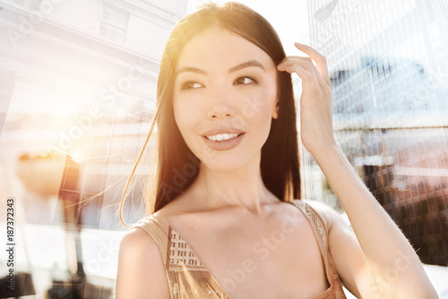 Staring aside. Beautiful brunette female keeping smile on face and raising left hand while touching her head Free Download Staring aside. Beautiful brunette female keeping smile on face and raising left hand while touching her head - GFXLoad