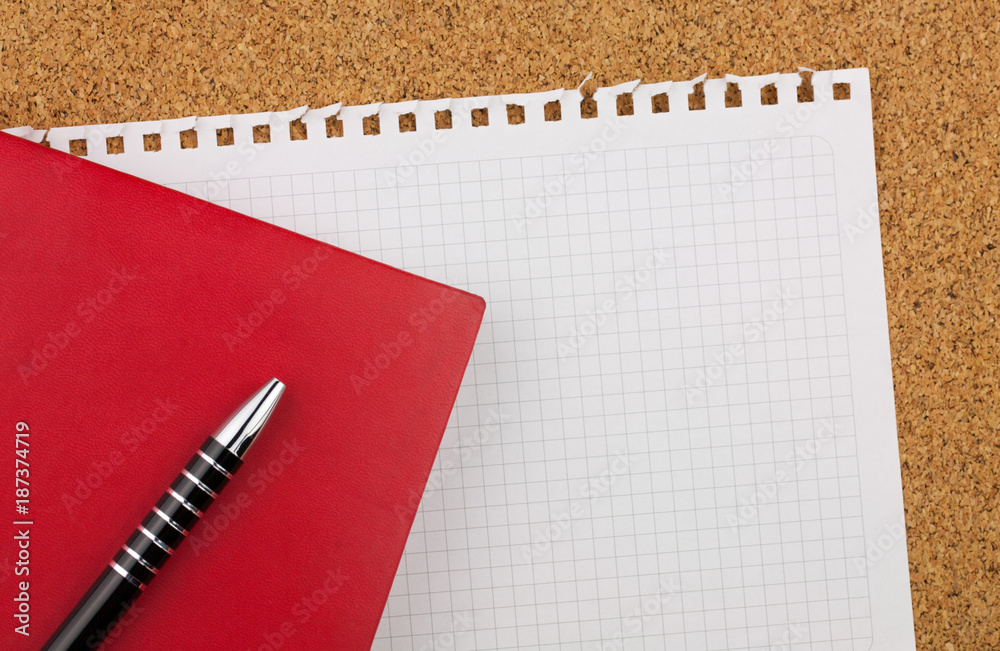 Empty square sheet of white paper wrested from notepad for your text. There are red notebook, black pen and cork board background. Empty square sheet of white paper wrested from notepad for your text. There are red notebook, black pen and cork board background.