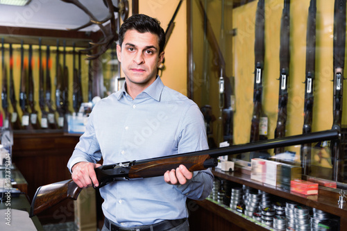 Handsome adult male in hunting shop with rifle in hands