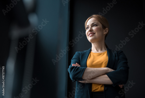 Low angle cheerful girl with crossing arms situating in apartment. Job concept photo