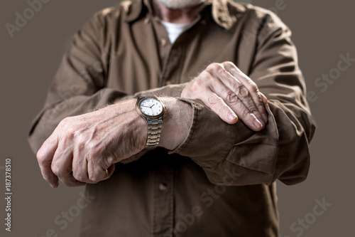 Man checking time on his wristwatch while showing it to camera. Isolated on grey background. Close up
