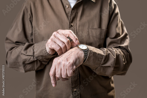 Senior arms pointing at the wristlet antique watch. Isolated on grey background. Close up