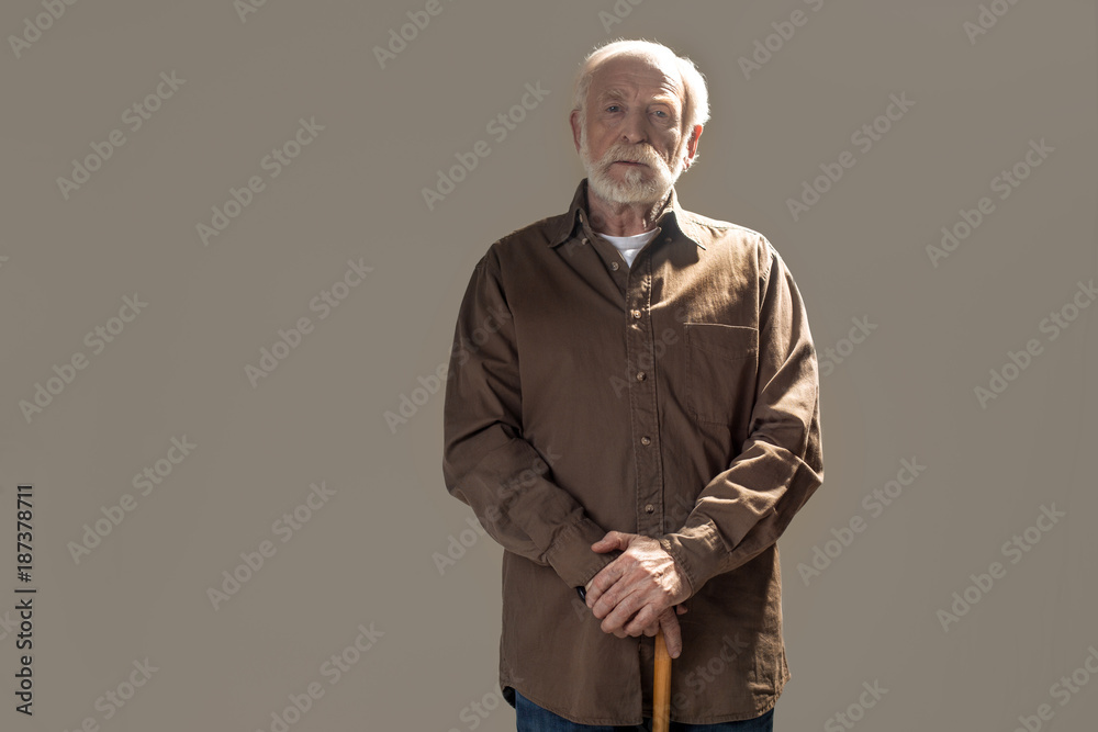 Waist up portrait of serious old man looking at camera with tranquility. Copy space in left side. Isolated on grey background