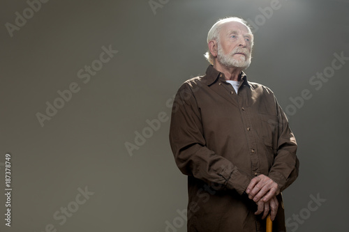 Elderly man with pensive face holding walking stick. Copy space in left side. Isolated on grey background