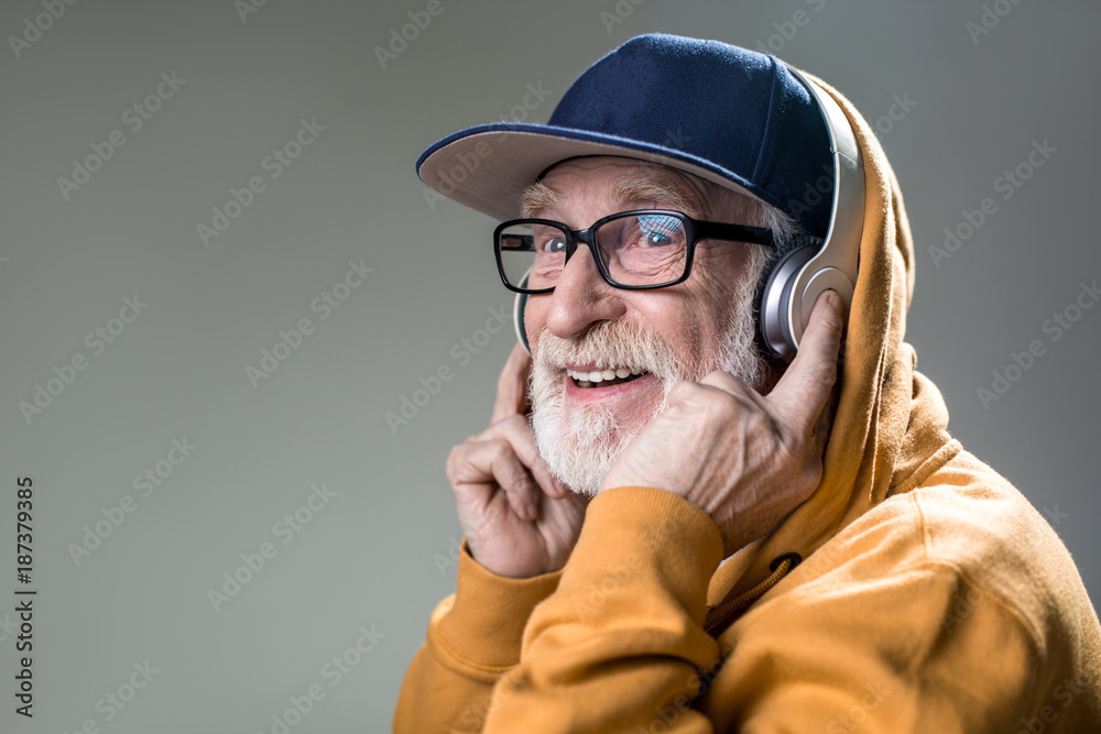 Happy old man with grin from ear to ear. He is wearing headphones over the  cap. Copy space in left side. Isolated on grey background Stock-Foto |  Adobe Stock