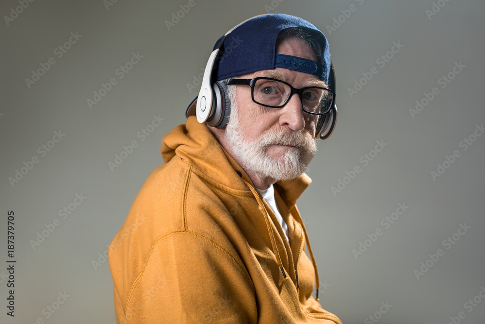 Calm pensioner wearing trendy clothing and headphones. Isolated on grey background Calm pensioner wearing trendy clothing and headphones. Isolated on grey background