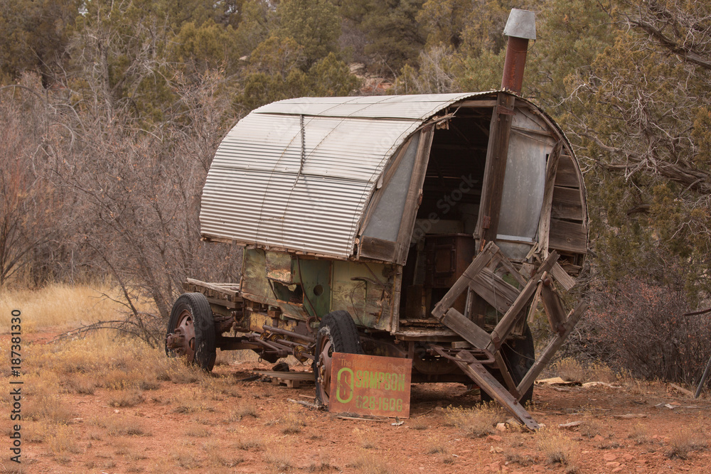 Old sheepherders wagon falling apart as it sits in a clearing on a winter day with a rusting old for sale sign leaning against the wheel