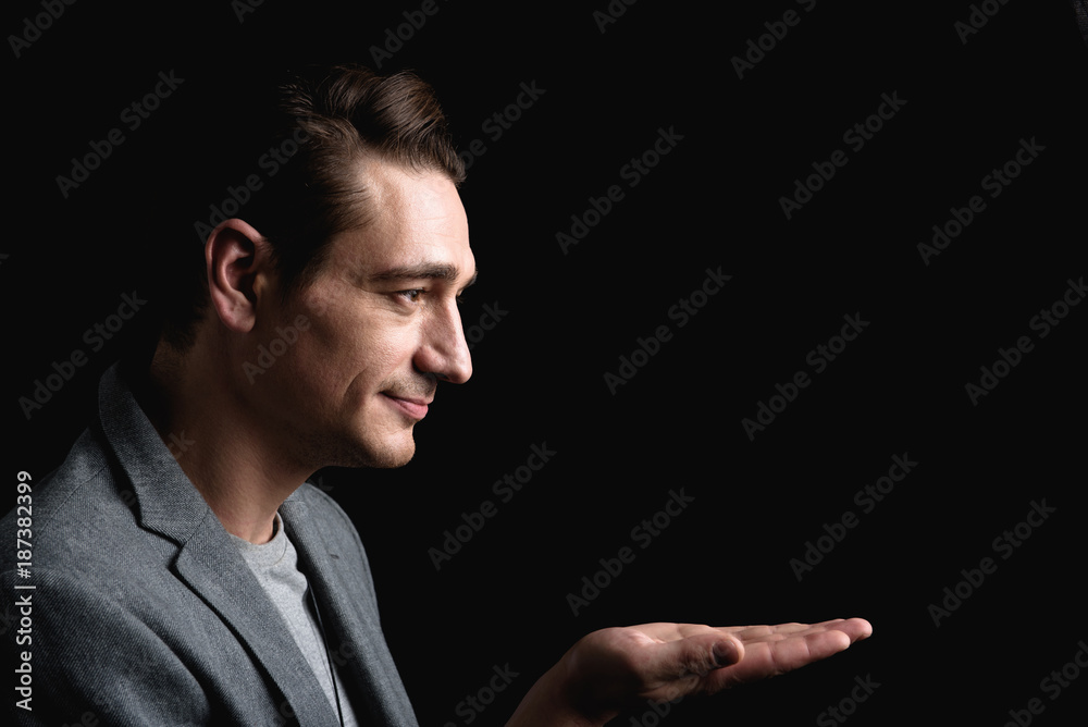 Look at this. Side view profile of stylish positive young attractive man is standing with smile while holding palm up. Isolated background and copy space in the right side Look at this. Side view profile of stylish positive young attractive man is standing with smile while holding palm up. Isolated background and copy space in the right side