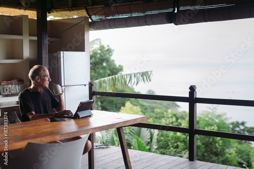 Mature man in his 60's working and traveling with tablet in trop photo