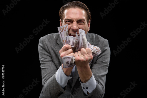 Passion about money. Portrait of adult crazy manager is standing and squeezing dollars in his fists while looking at camera with obsess. Isolated background