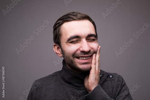 Closeup portrait of young man with tooth ache crown problem about to cry from pain touching outside mouth with hand, isolated on dark background. Negative human emotion facial expression feeling
